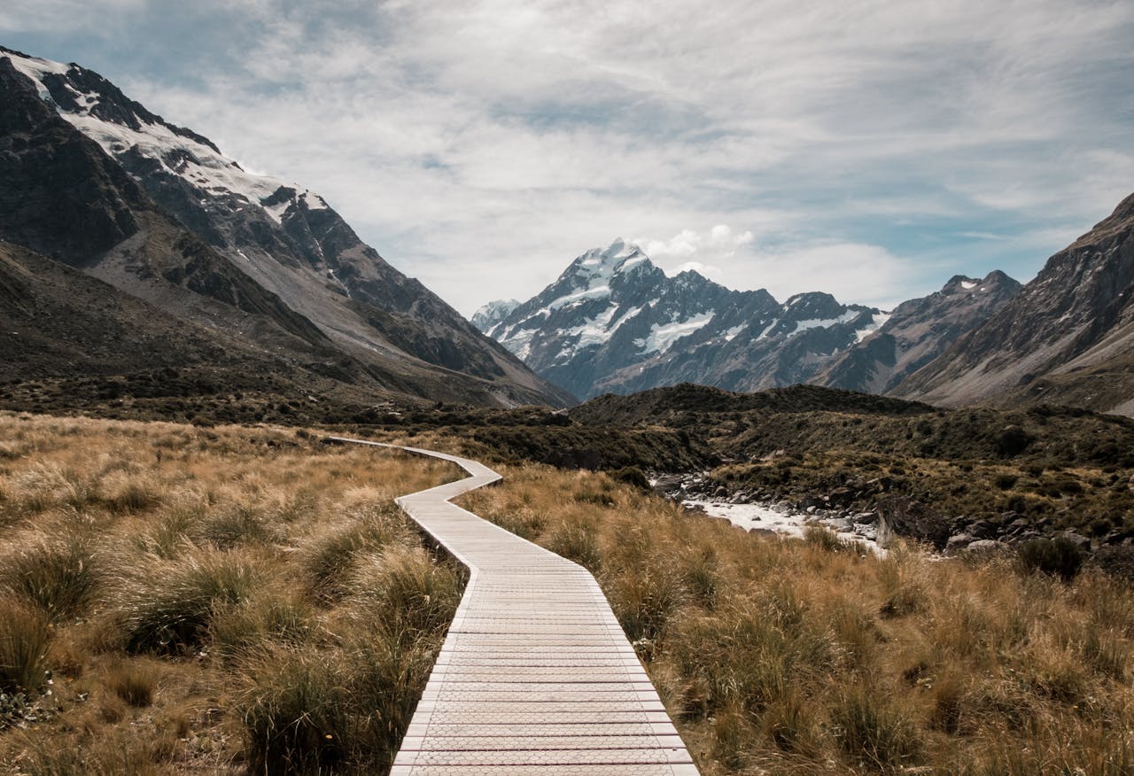 About Wooden walkway leads through rugged landscape towards majestic snow-capped mountains.